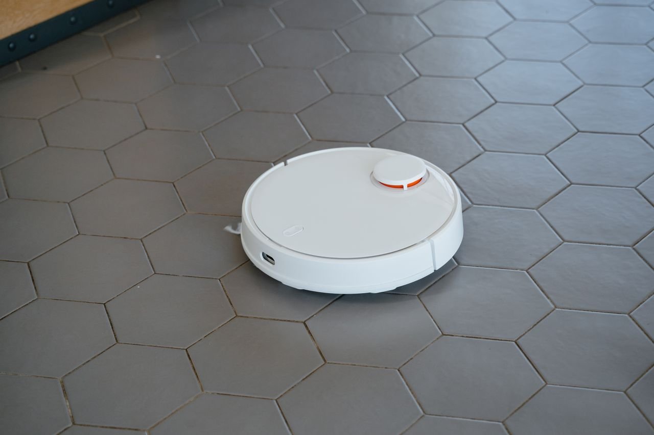 A sleek, white robotic vacuum cleaner operating on a hexagonal tiled floor.